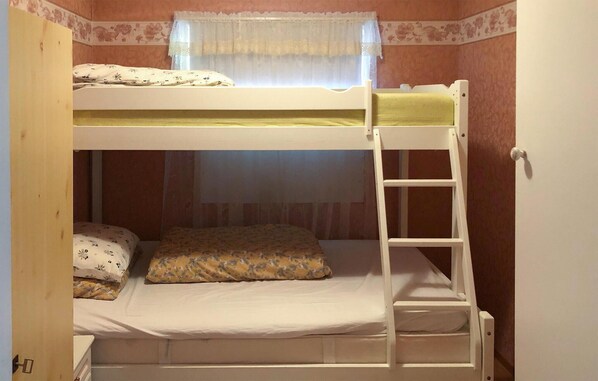 A bunk bed with a ladder, a window with lace curtains, and a floral-patterned bedspread.