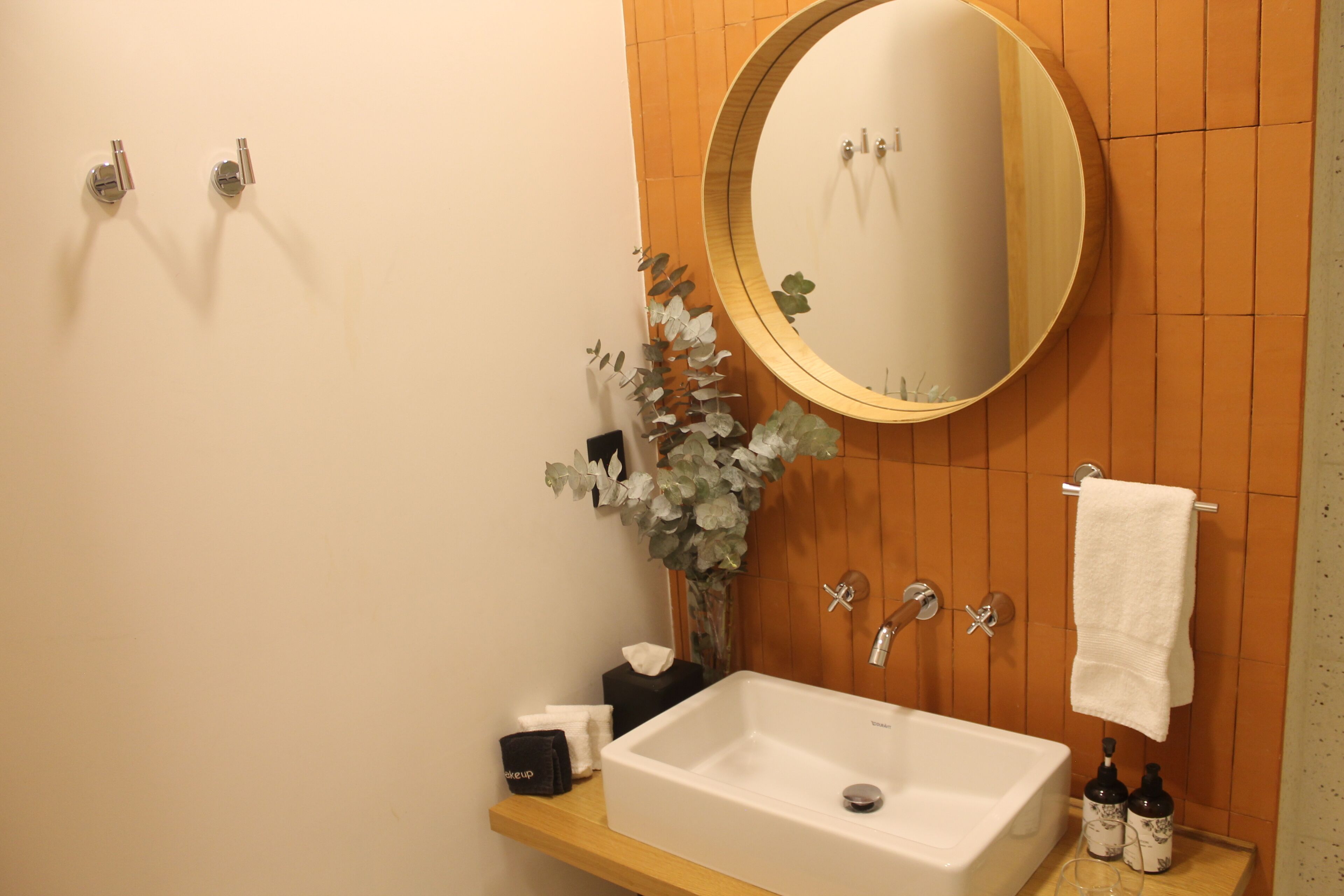 A bathroom with a white sink, a round mirror, a wooden panel wall, and a towel hanging on the wall.