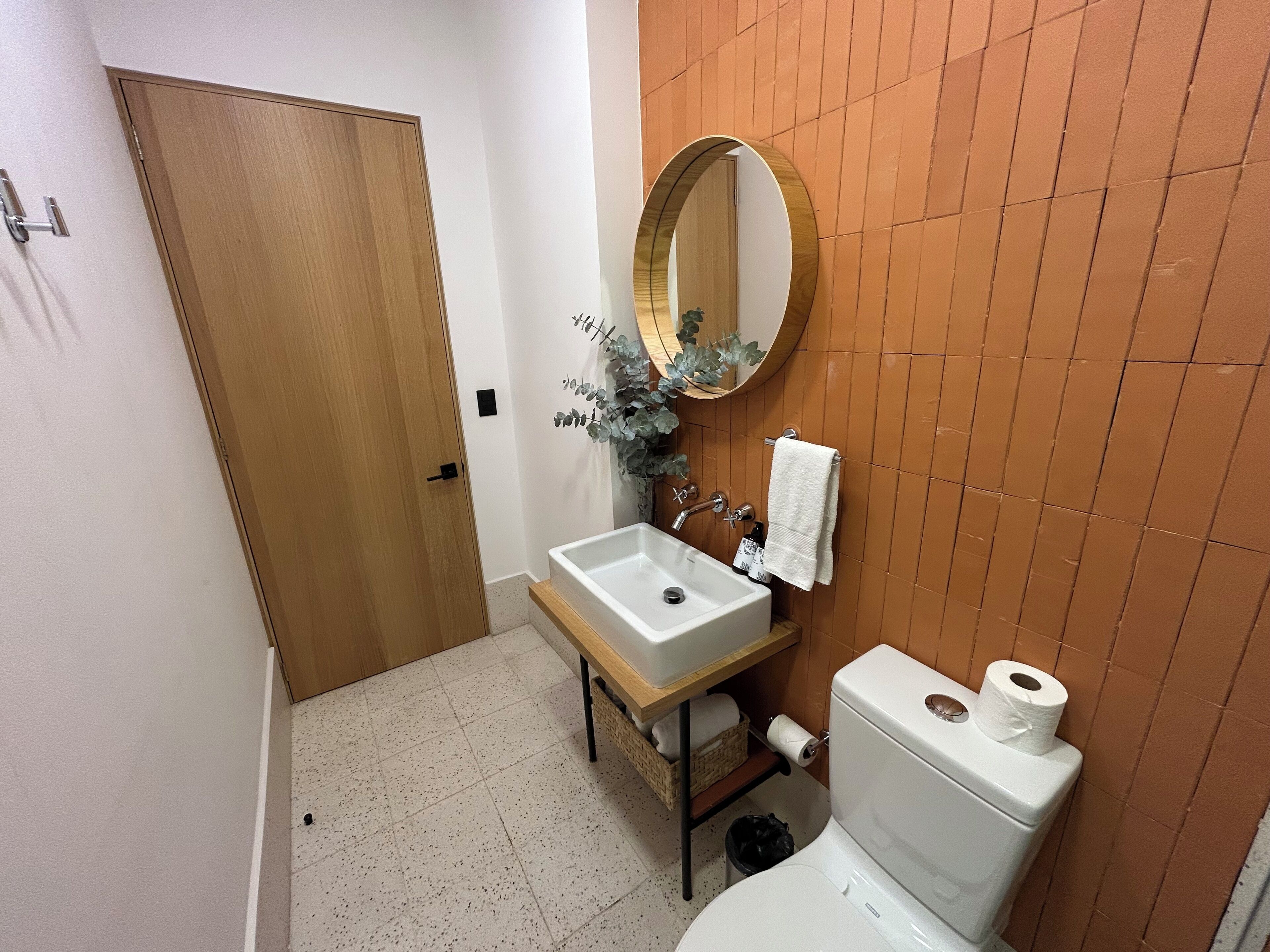 A bathroom with a wooden door, a white sink with a mirror, a toilet, and a towel rack.