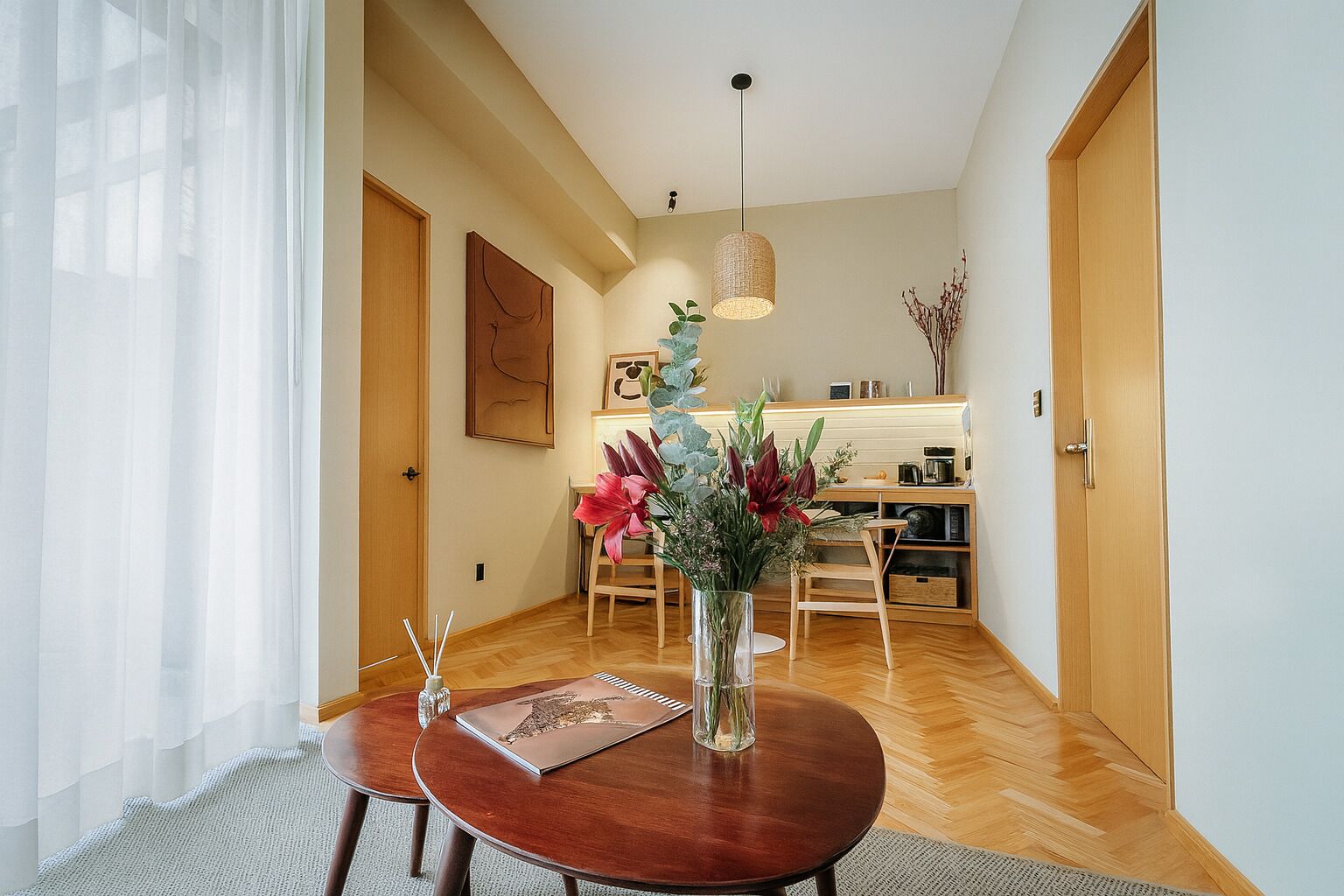 Un comedor con una mesa redonda de madera, sillas, un florero con flores y una lámpara colgante.