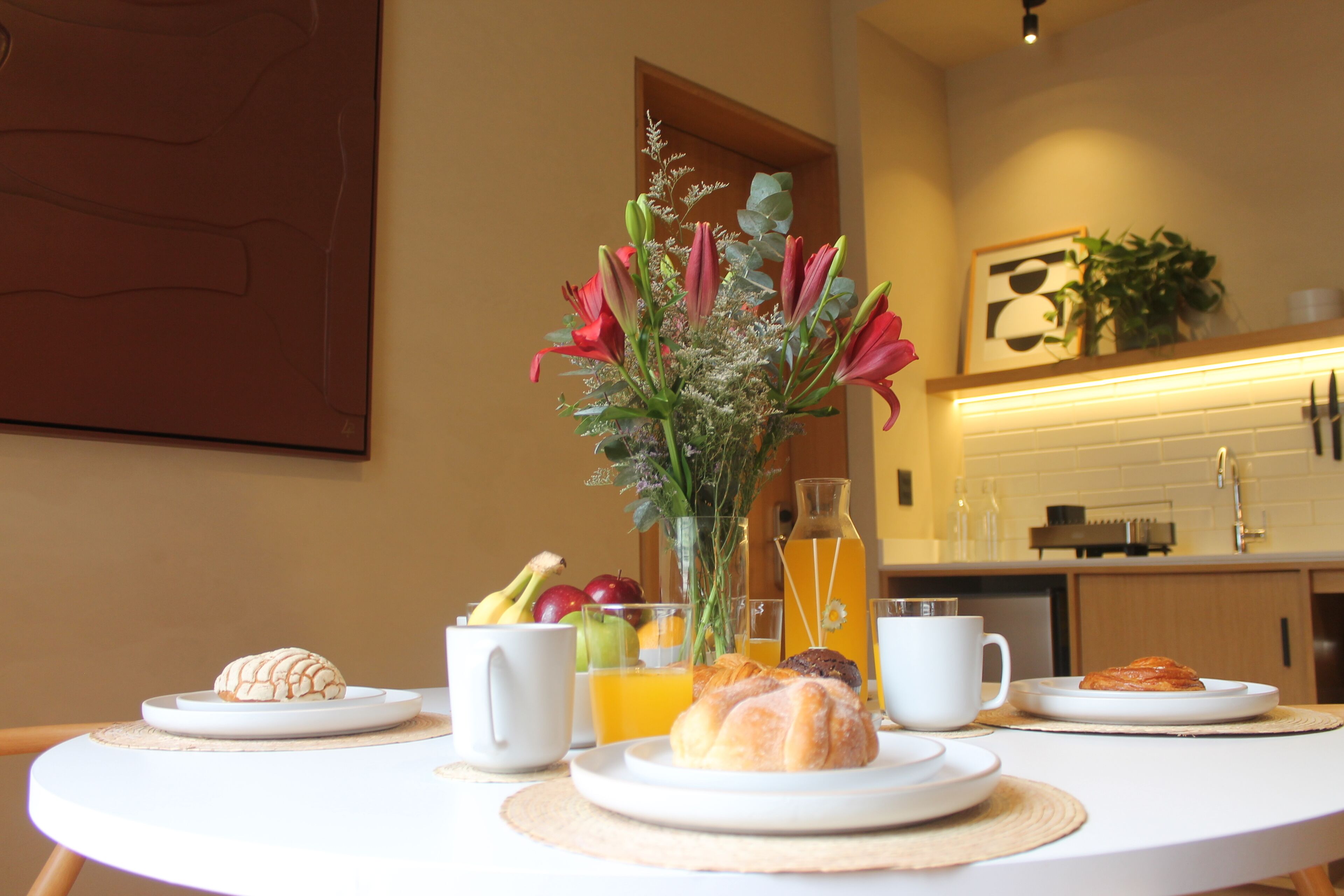 Une table de petit-déjeuner avec des croissants, des fruits et un vase rempli de fleurs.