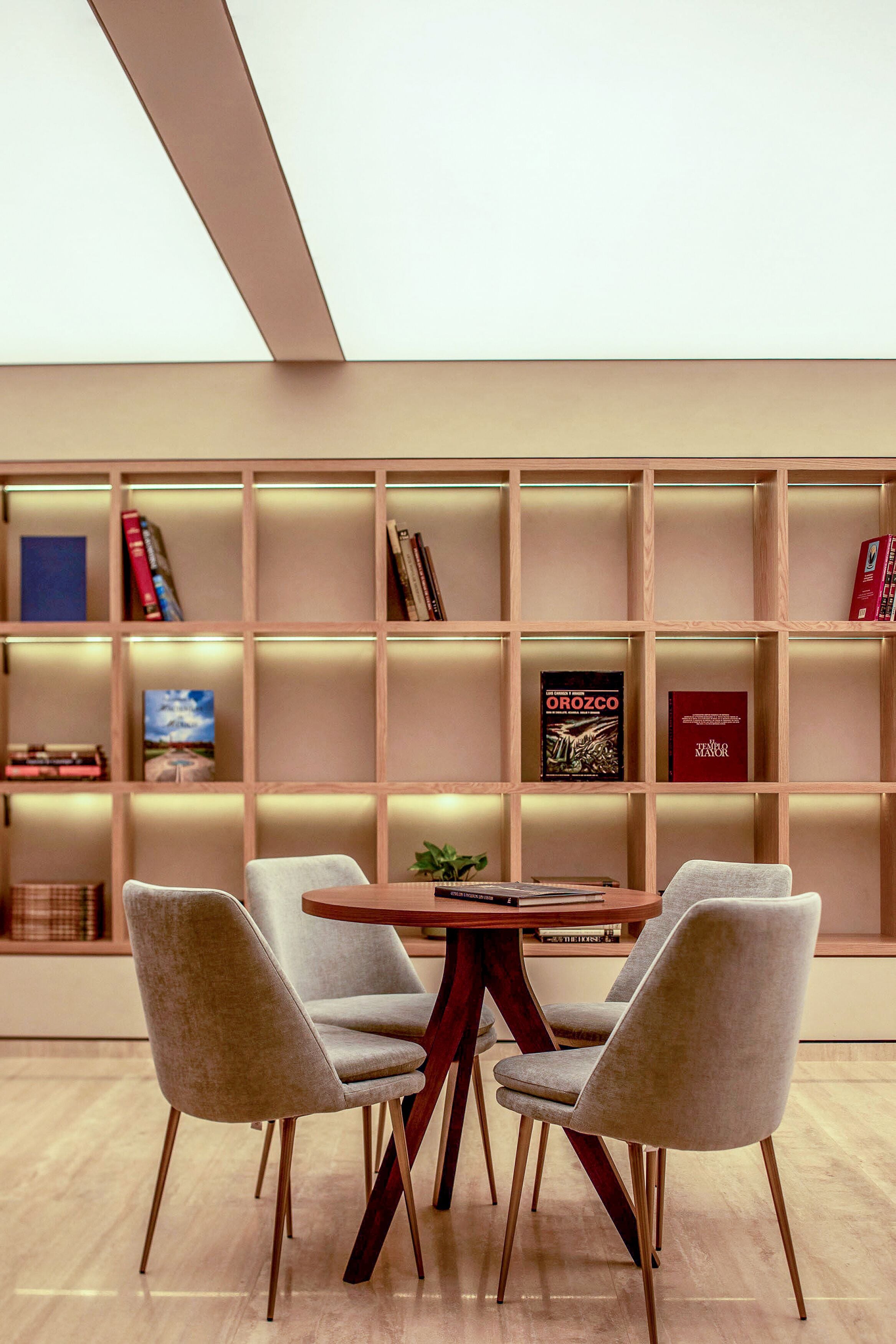 A modern dining area with a wooden table and two chairs, a bookshelf with books and decorative items, and a wooden floor.
