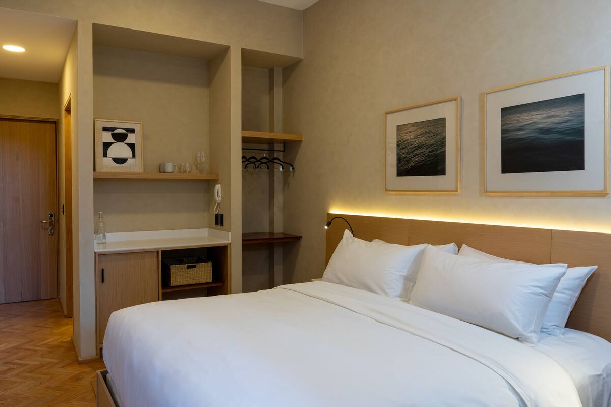 Ein Hotelzimmer mit Bett, Schreibtisch und Kleiderschrank. An der Wand hängen zwei gerahmte Bilder.