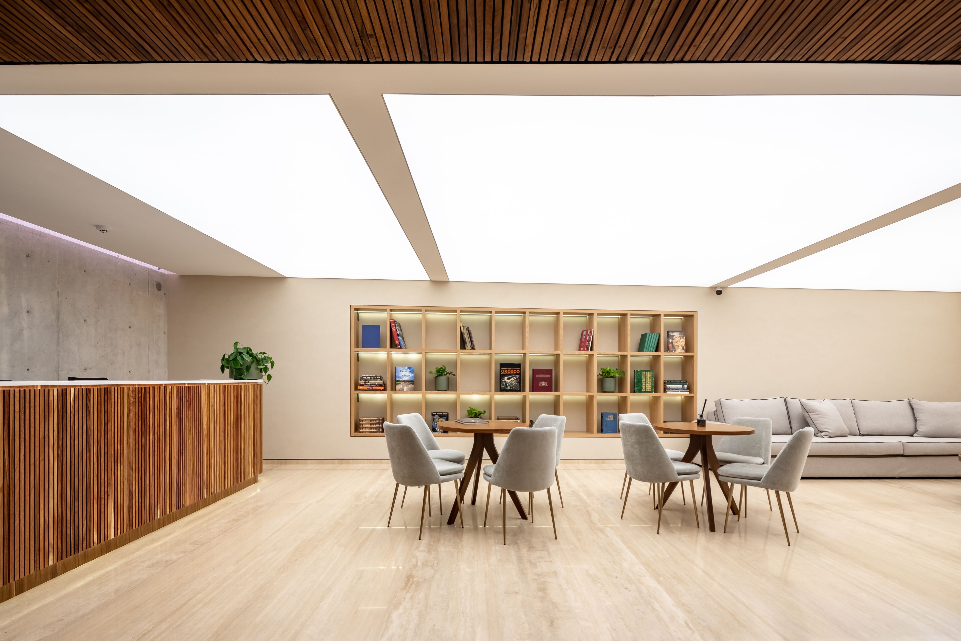 A modern reception area with a wooden reception desk, a round table with chairs, a bookshelf, and a sofa.