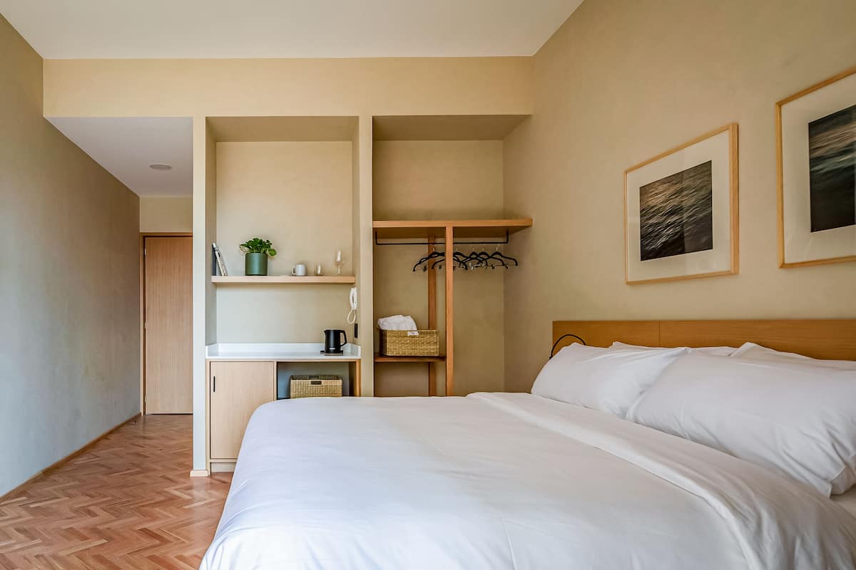 Ein Schlafzimmer mit einem Bett, einem Kleiderschrank, einem Regal mit einer Pflanze und einem gerahmten Bild an der Wand.