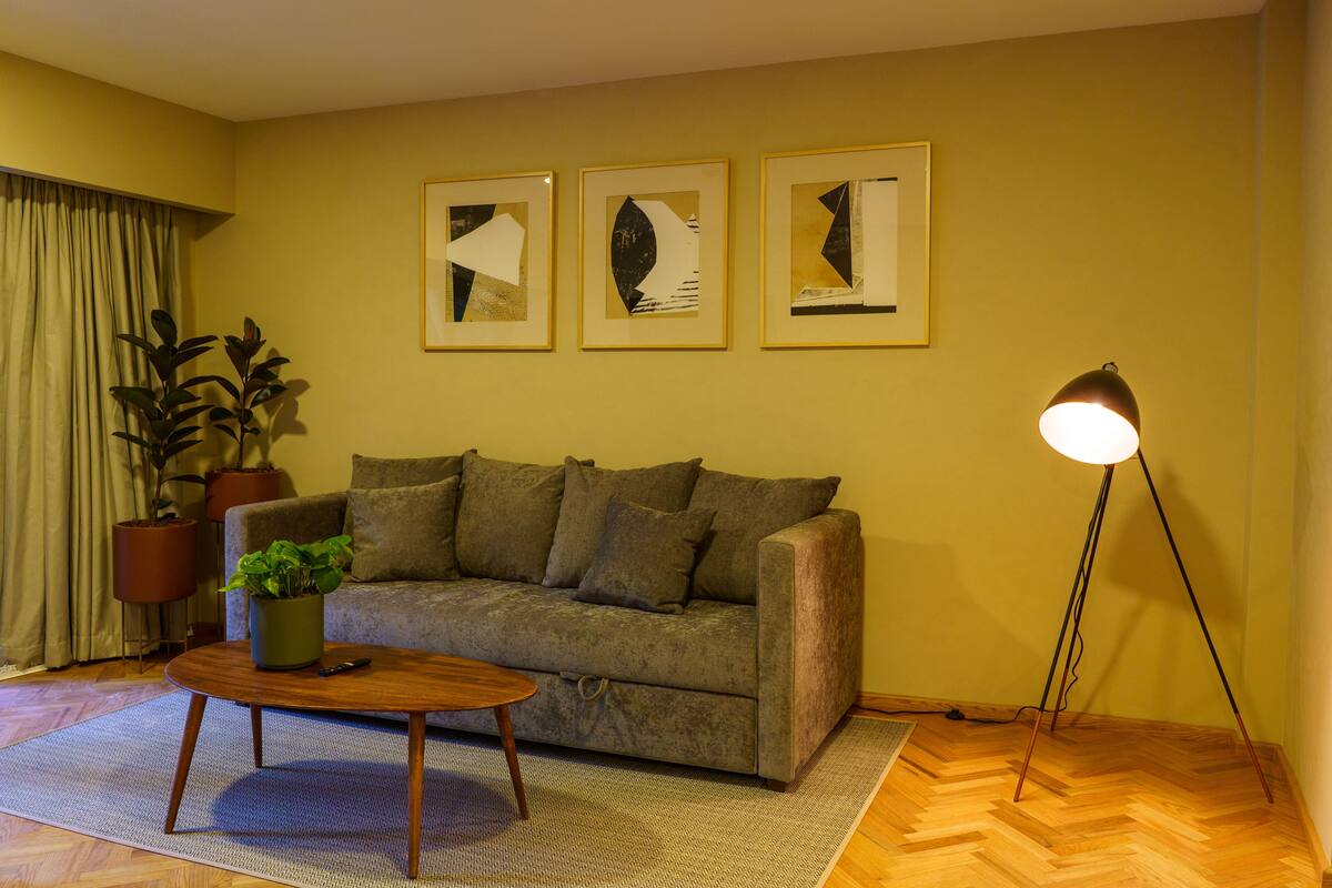 Ein Wohnzimmer mit einer Couch, einem Couchtisch, einer Stehlampe und drei gerahmten Kunstwerken an der Wand.