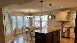 A kitchen with a central island, wooden cabinets, a dining area with chairs, and a chandelier. - CENTER OF OCEAN CITY - Walk to Beach/Boards/Downtown (Ocean City)