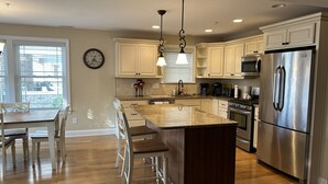 A modern kitchen with white cabinetry, a large island, stainless steel appliances, and a dining area with a wooden table and chairs. - CENTER OF OCEAN CITY - Walk to Beach/Boards/Downtown (Ocean City)