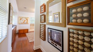 A hallway with framed artwork, a display of signed baseballs, and a framed photograph on the wall. - Beautiful Spanish Style Home In The Heart of Coral Gables (Coral Gables)