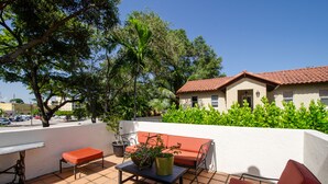 An outdoor patio with a table, orange sofa, and potted plants. - Beautiful Spanish Style Home In The Heart of Coral Gables (Coral Gables)