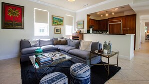 A living room with a sectional sofa, a coffee table, and a small side table. There is a kitchen area visible in the background. - Beautiful Spanish Style Home In The Heart of Coral Gables (Coral Gables)