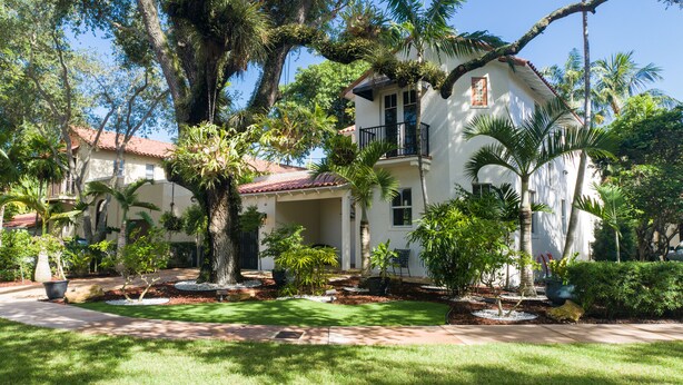 A two-story house with a covered patio, surrounded by lush greenery and palm trees. - Beautiful Spanish Style Home In The Heart of Coral Gables (Coral Gables)