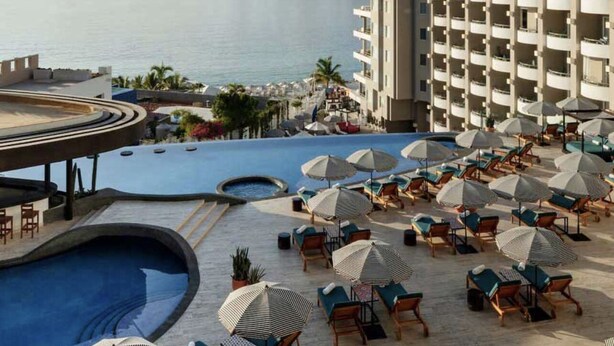 Zona de piscina d'un resort amb nombroses gandules i ombrelles, una piscina gran i vistes al mar i a les muntanyes.