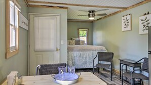 Un dormitorio con una cama, una mesa de comedor con sillas, un ventilador de techo y cuadros en la pared.