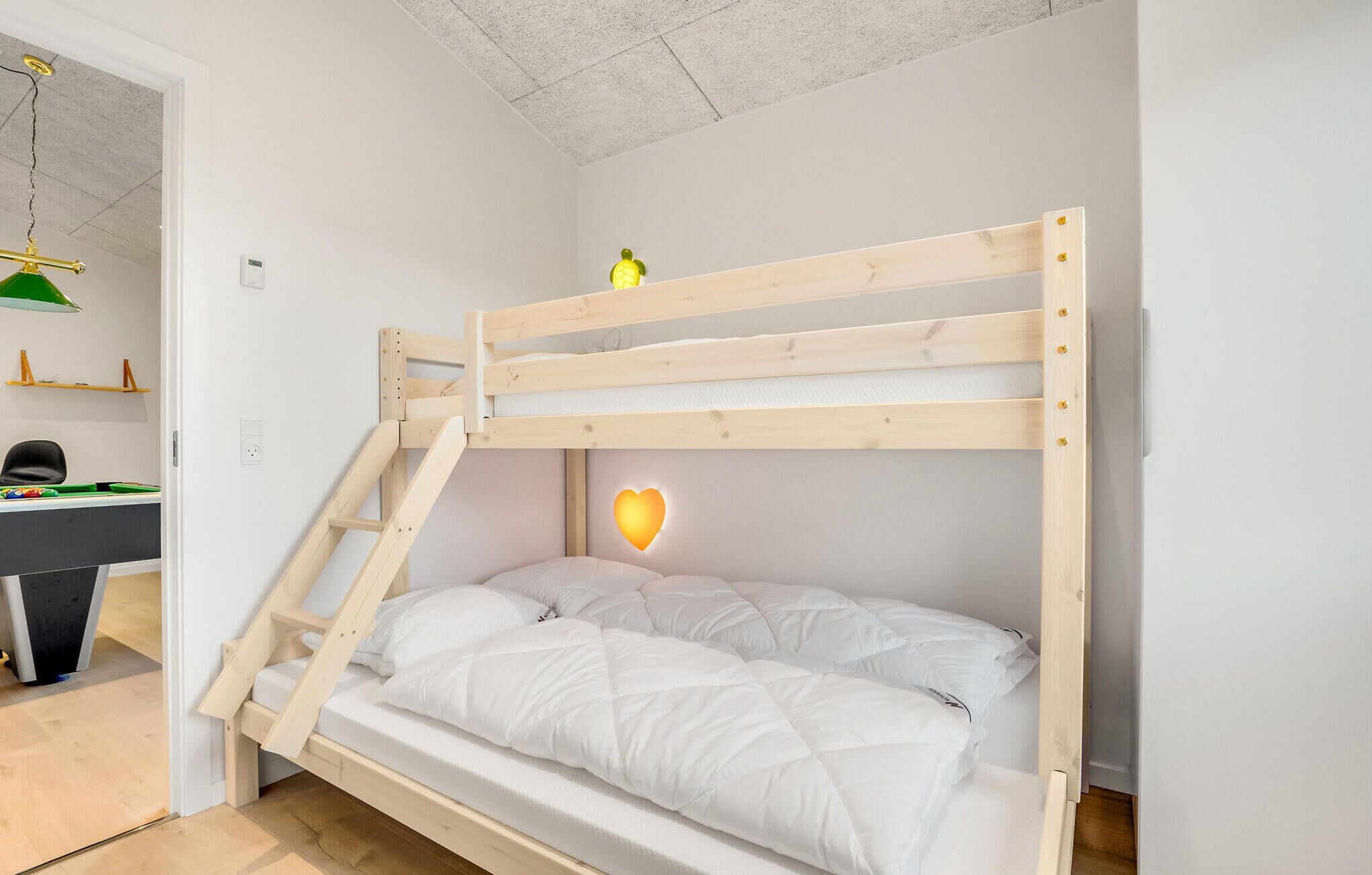 Un lit superposé avec une échelle, un bureau avec une table de billard verte et un luminaire en forme de cœur fixé au mur.