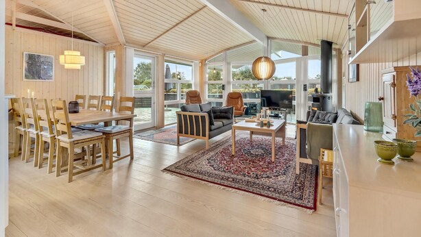 Amplia sala de estar con techo alto, muebles de madera, alfombra grande y televisor.
