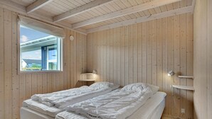 Habitación con dos camas, paredes de madera, una ventana y un estante pequeño.