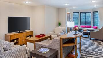 A modern living room with a flat-screen TV, a wooden cabinet, a sofa, a coffee table, and a patterned rug.