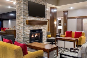 A modern living room with a fireplace, a flat-screen TV mounted on a stone wall, and a seating area with sofas and a coffee table.