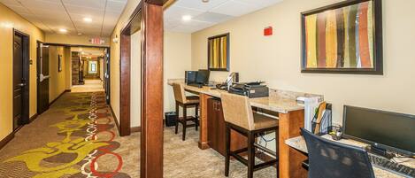 A hotel lobby with a carpeted hallway, a reception desk, computers, and a framed artwork on the wall.