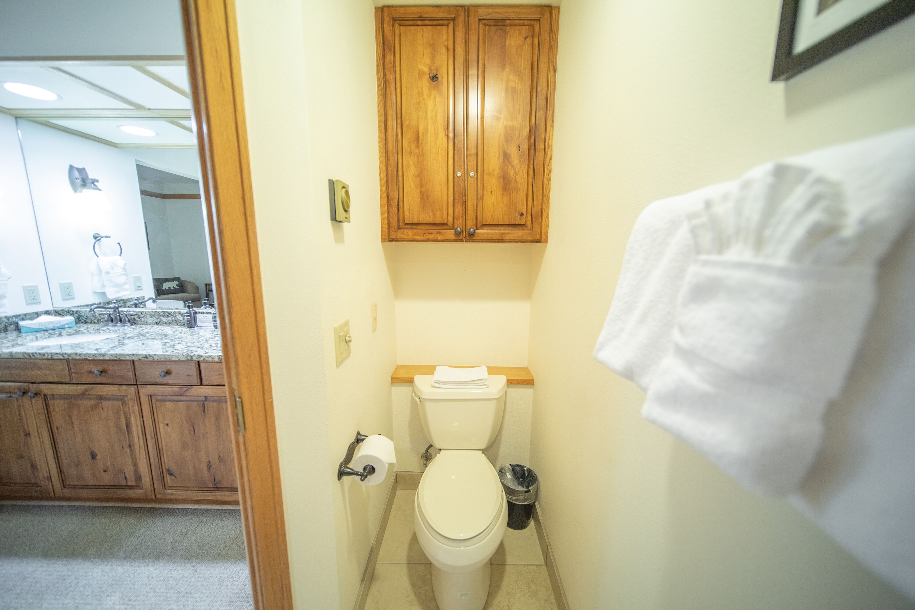 A bathroom with a toilet, wooden cabinets, and a towel hanging on the wall.