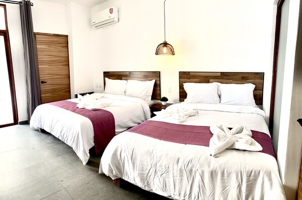 A hotel room with two beds, each with white bedding and a wooden headboard. There is a hanging light fixture above the beds.