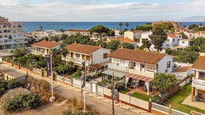 Zona residencial costera con casas de paredes blancas y tejados de tejas rojas, rodeada de vegetación y con vistas despejadas al mar.