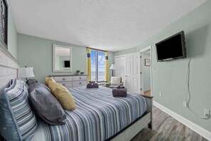 A bedroom with a bed, a dresser, a TV, and a window with curtains. - Bright Oceanfront 1br,King,Pool,Sm Dogs,W54 (Myrtle Beach)