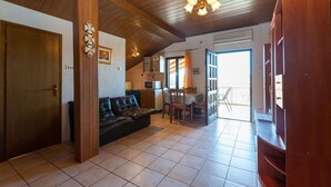 Ein gemütliches Wohnzimmer mit Holzboden, einer schwarzen Ledersofa, einem Esstisch mit Stühlen und einer Küchenzeile mit Mikrowelle.