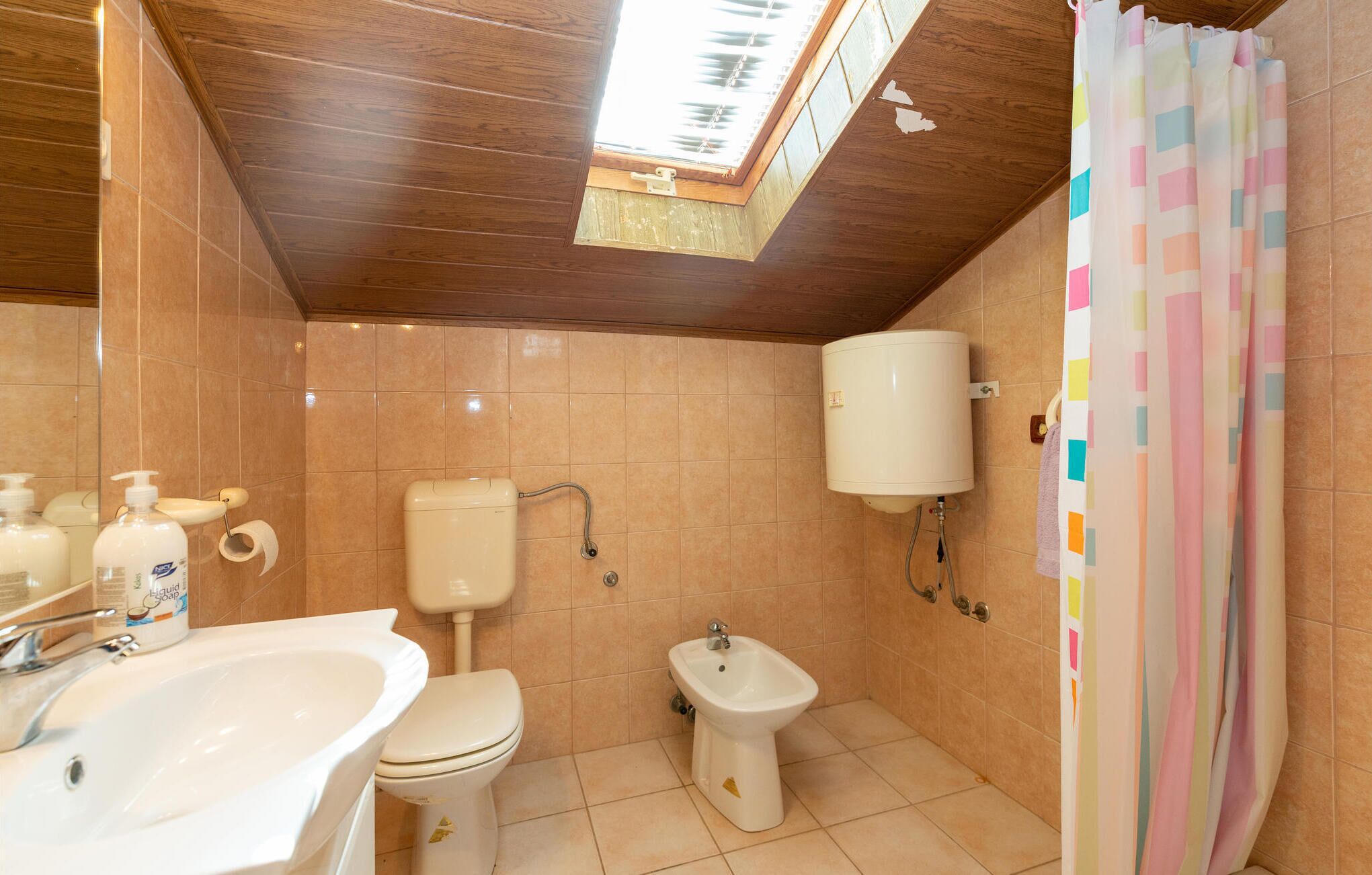 Ein Badezimmer mit Dachfenster, Toilette, Bidet, Waschbecken und Duschvorhang.