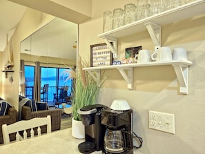 A cozy kitchen with a coffee maker, a sign that reads "COFFEE IS BETTER AT THE LAKE", and a view of the lake through large windows.