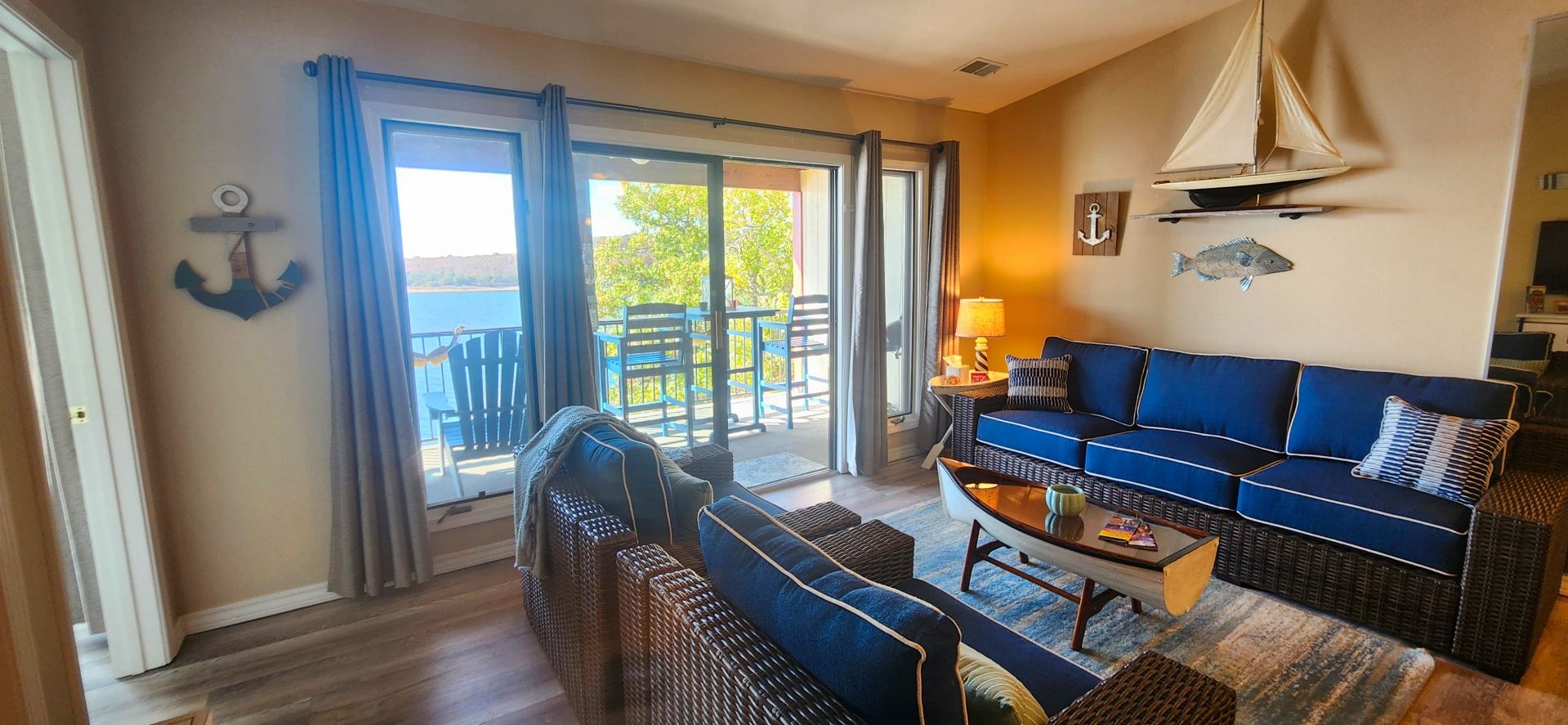 A living room with a sofa, coffee table, and chairs, a balcony with a view of the water, and nautical decor.