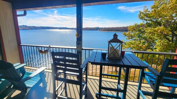 Un balcon donnant sur un lac, une table avec une lanterne et des chaises bleues.