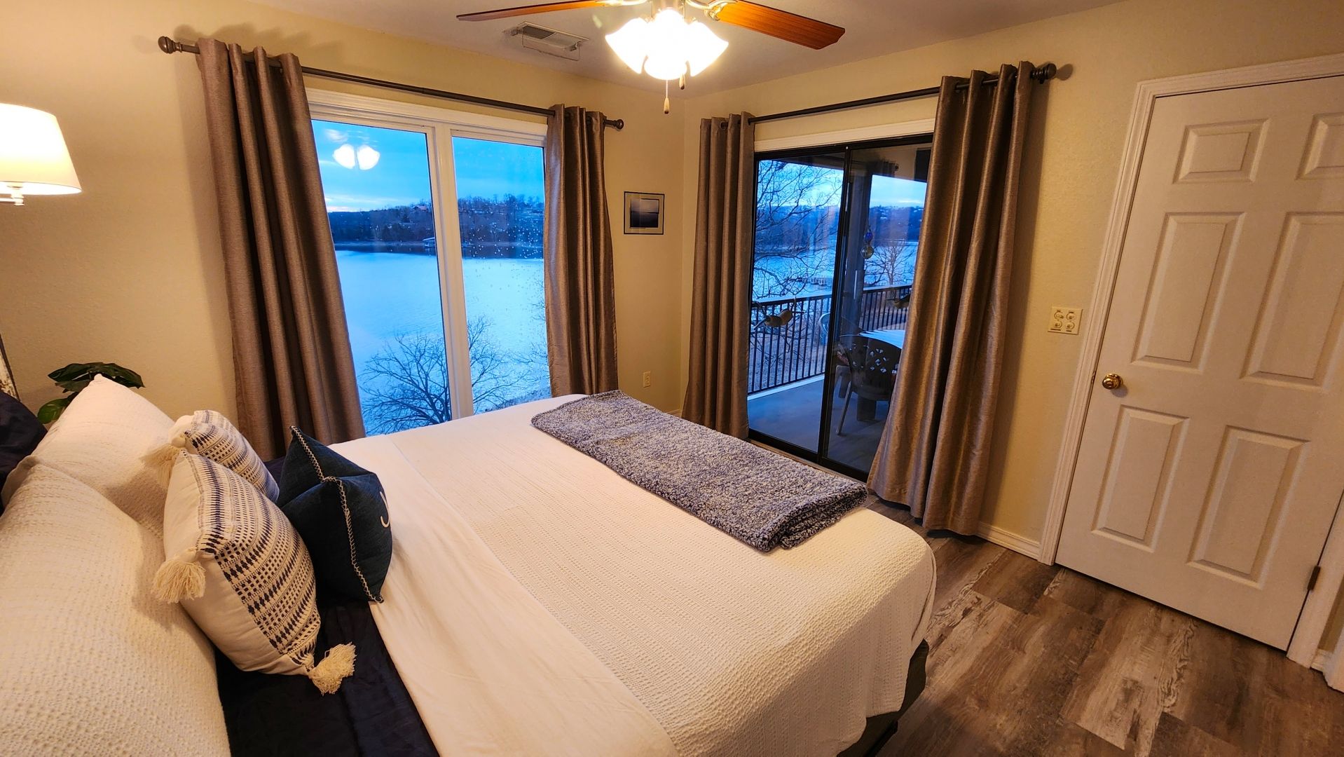 A bedroom with a bed, a nightstand, a lamp, and a view of a snowy landscape through large windows.