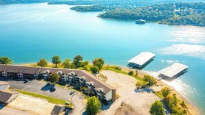 Vue aérienne d’un hôtel situé au bord d’un lac, avec un parking, des bâtiments et des zones d’amarrage.