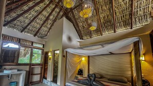 A room with a bed, a small desk, a window, and a thatched ceiling.
