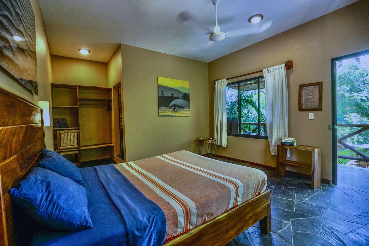 Quarto com cama, guarda-roupa, janela com cortinas e vista para o verde lá fora.