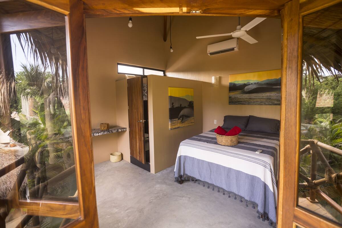 Quarto com uma cama, ventoinha no teto e um quadro na parede.