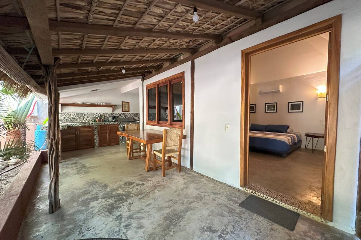 Um quarto amplo com uma cama grande, uma mesa de jantar de madeira e uma cozinha com fogão e armários.