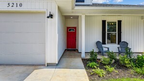 Uma casa branca com garagem, porta vermelha e duas cadeiras Adirondack no alpendre.