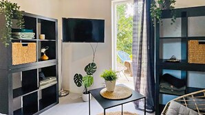 A modern living room with black shelving units, a flat-screen TV, a small table with a plant, and a view of the outdoors through a glass door. - Amazing home in Ronneby with WiFi (Ronneby)