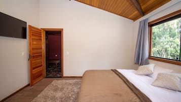 A bedroom with a bed, a TV, a window with a view of trees, and a wooden ceiling.