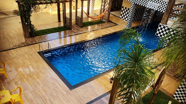 A swimming pool with a checkered border, surrounded by wooden decking and a small grassy area. - Pousada Evolução engenho (Nova Lima)
