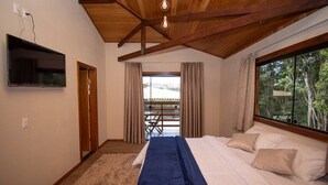A bedroom with a bed, a TV mounted on the wall, a wooden ceiling, and a window with curtains. - Pousada Evolução engenho (Nova Lima)