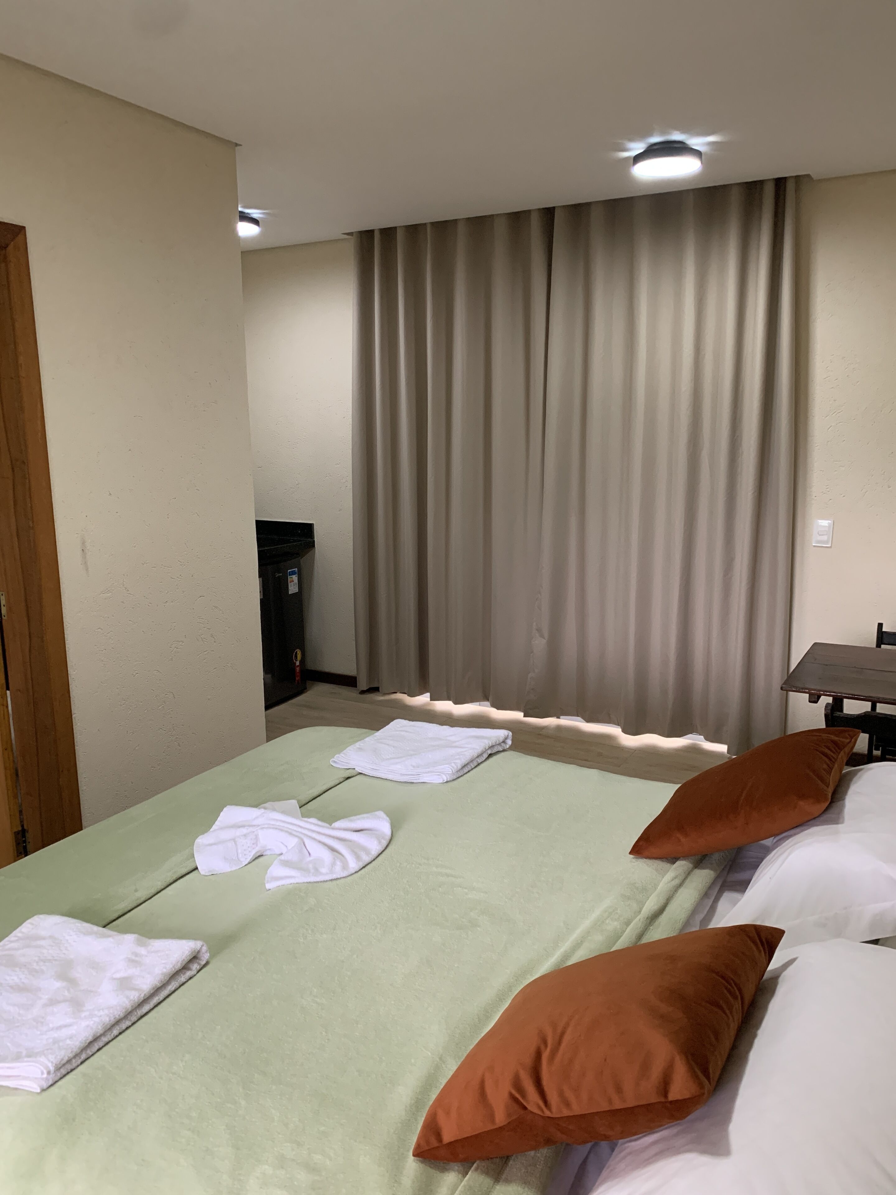 Una habitación de hotel con cama, almohadas, una mesa y una cortina.