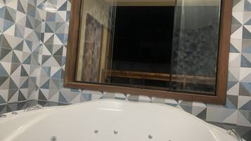 Un baño con una bañera blanca, azulejos de diseño geométrico y un espejo con marco de madera.