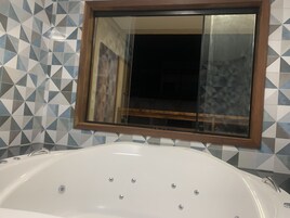 Un baño con una bañera blanca, azulejos de diseño geométrico y un espejo con marco de madera.