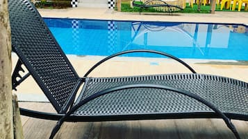 Uma cadeira de lounge preta ao lado de uma piscina, com um muro xadrez e uma rede ao fundo.