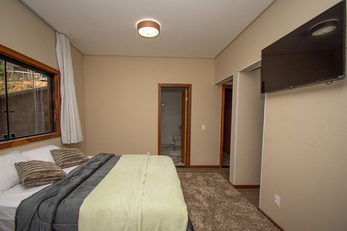 A bedroom with a bed, a TV mounted on the wall, and a door leading to another room.