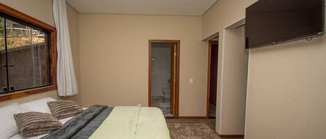 A bedroom with a bed, a TV mounted on the wall, and a door leading to another room.